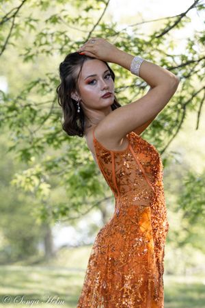 An elegant orange sequined dress stands out against lush green foliage in an outdoor portrait.