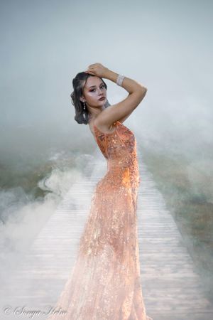A dreamy portrait on a misty boardwalk features a shimmering peach-colored evening gown.