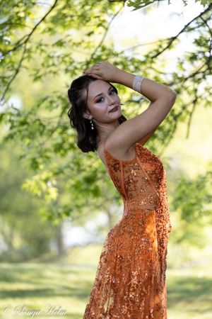 An elegant pose captured in natural sunlight showcases a stunning orange sequined formal dress.
