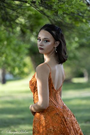 A stunning orange formal dress is showcased against lush green foliage in an outdoor portrait.