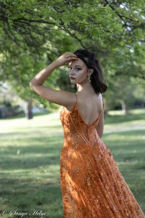 A backlit portrait features a flowing orange sequined gown in a serene garden setting.