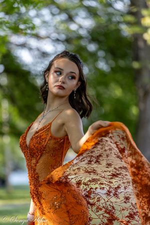 A flowing orange sequined dress catches movement in a dynamic outdoor portrait.