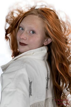 A person with flowing red hair wearing a white coat glances over their shoulder in an artistic portrait.