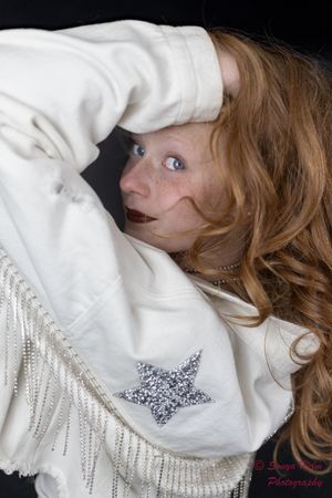 A vintage inspired portrait features a white fringed sweater with a sparkly star detail against a dark background.