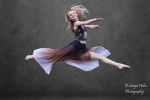 A dancer leaps through the air with outstretched arms in a dynamic dance sequence against a gray backdrop.
