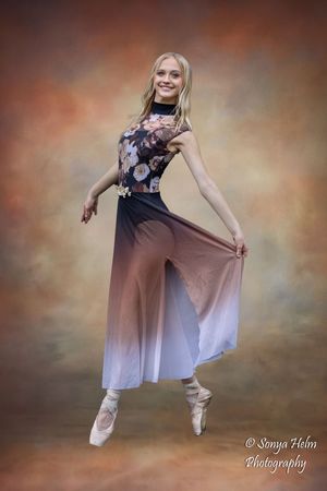 A ballet dancer in pointe shoes performs an elegant pose wearing a flowy ombre dress against a dreamy background.