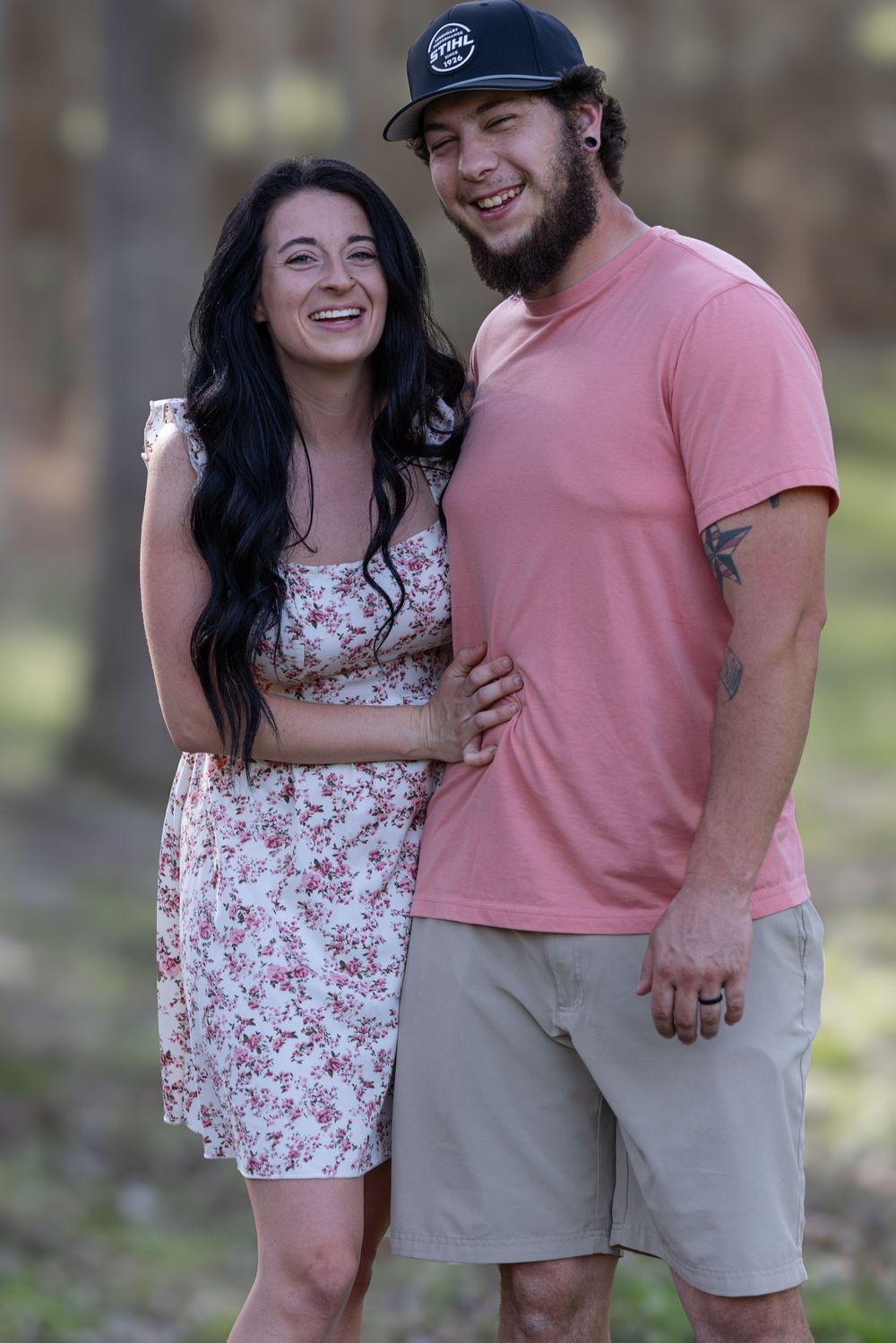 A couple shares a laugh while standing together outdoors, wearing summer clothing and expressing joy.
