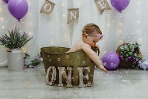 Baby girl sitting in vintage metal tub during ONE first birthday photo shoot.