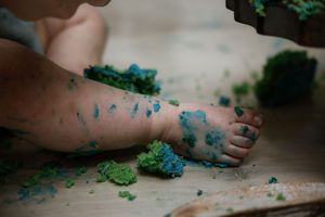 Close-up of baby feet and legs with colorful cake smash frosting on wooden surface.