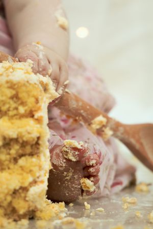Close-up of a baby's hands and feet covered in cake crumbs during a first birthday cake smash.