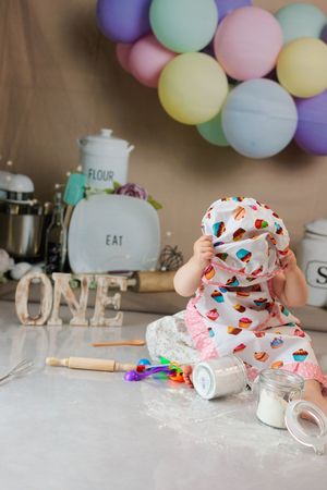 Baby in cupcake outfit playing on flour-covered surface at first birthday cake smash setup.