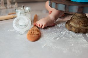 Close-up of baby feet near engraved wooden spoon on flour-dusted surface during cake smash.