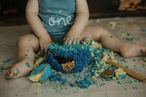 Baby in 'one' shirt smashing a blue Cookie Monster first birthday cake during a cake smash photoshoot.