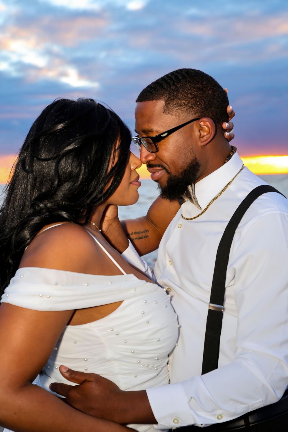 Romantic sunset photoshoot featuring tender moments against cloudy sky backdrop.