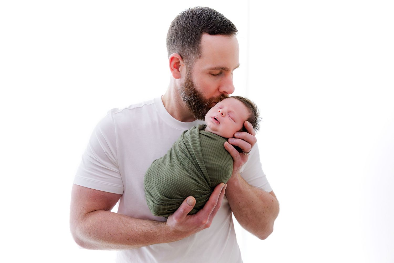 A tender moment between parent and newborn baby in a minimalist white studio setting.