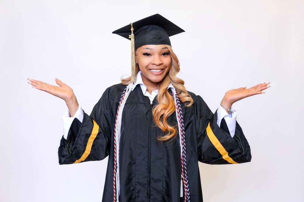 Graduate in black cap and gown poses expressively against white background.
