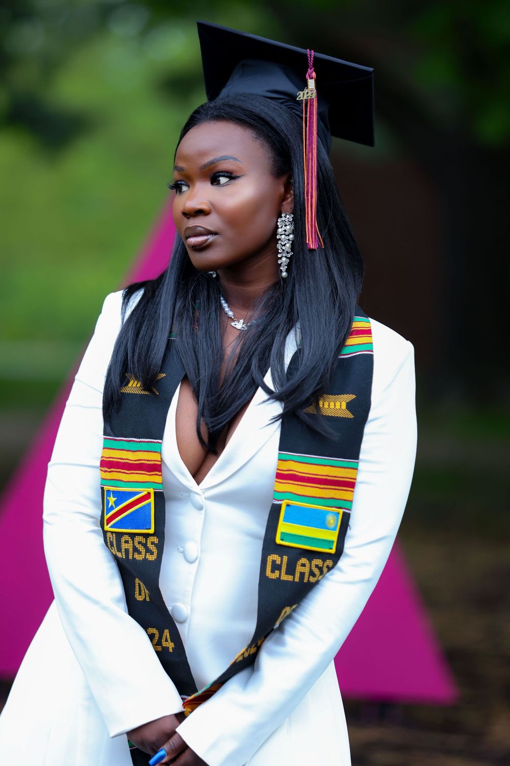 Graduate wearing traditional cap and gown with colorful cultural stole during outdoor photo session.