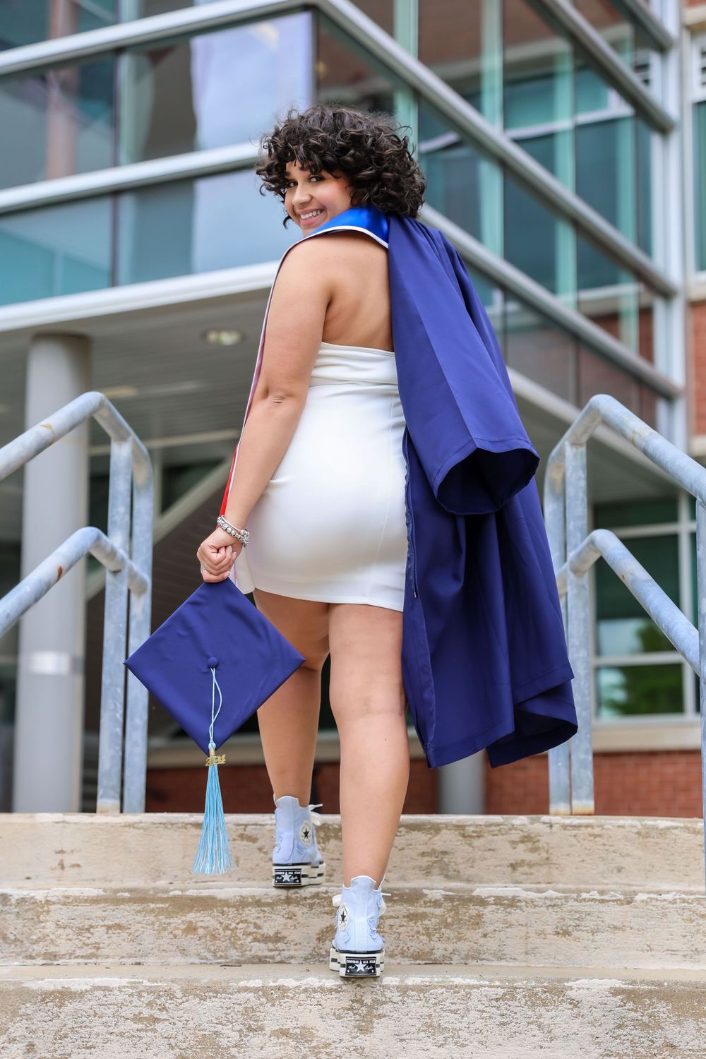 Close-up of feet on stairs showing white sneakers and blue graduation gown during a celebratory photoshoot.
