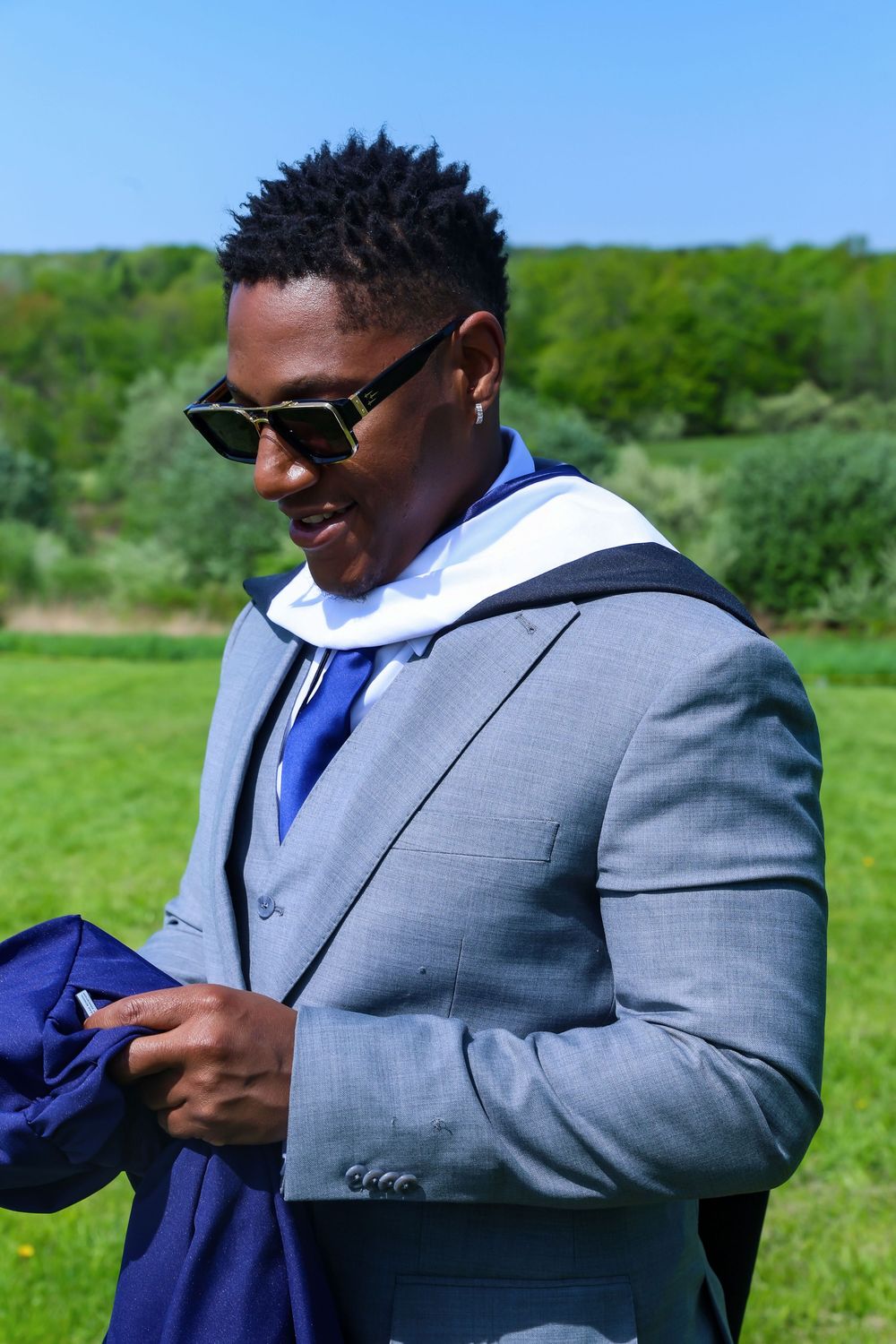 Person in grey suit with blue tie stands in sunny green field.