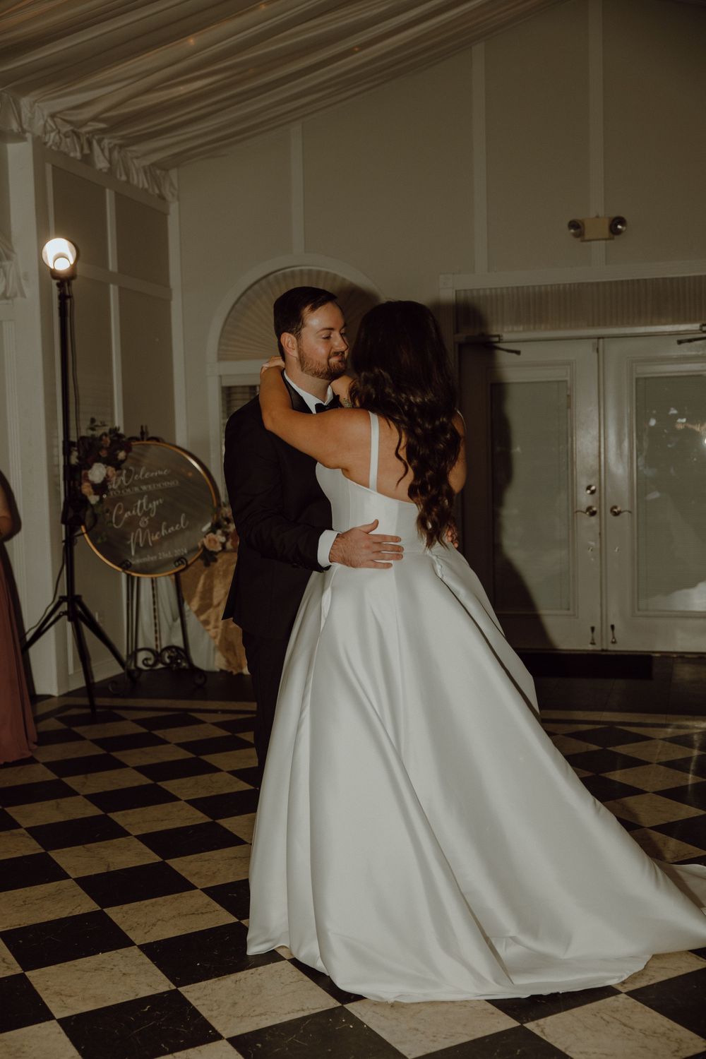 A couple dancing in formal attire on a checkered floor at their wedding reception.
