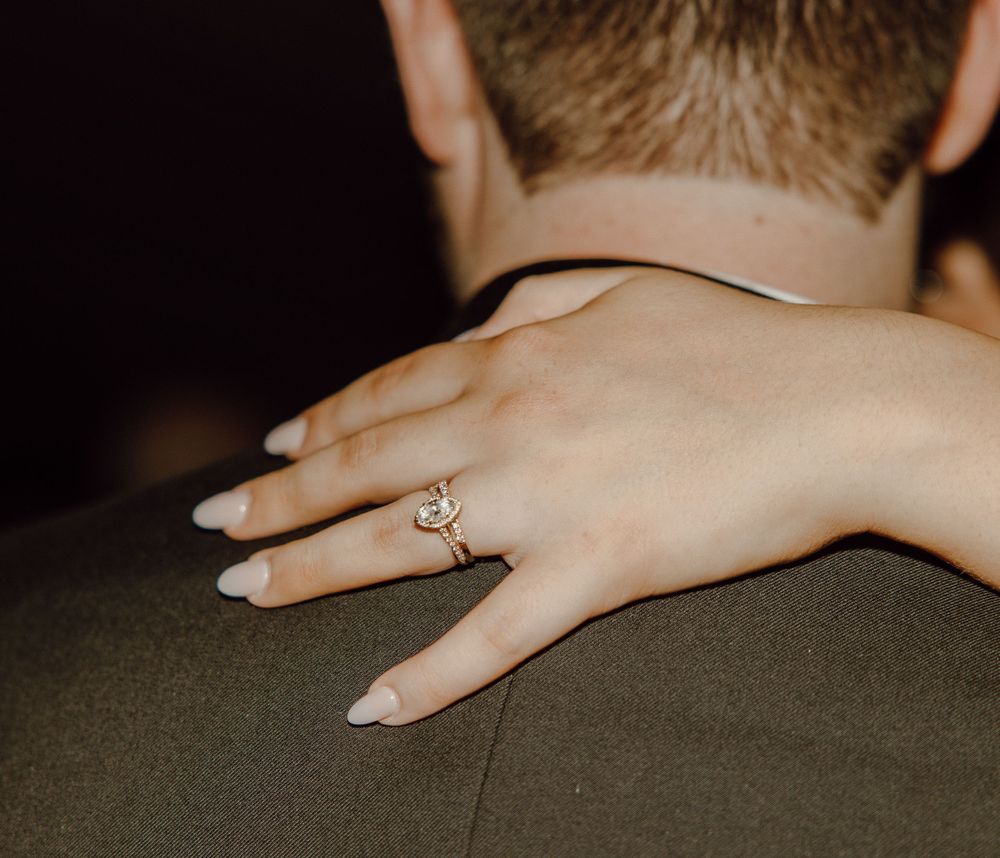 Close-up of hands with wedding rings resting on a dark surface during an intimate moment.