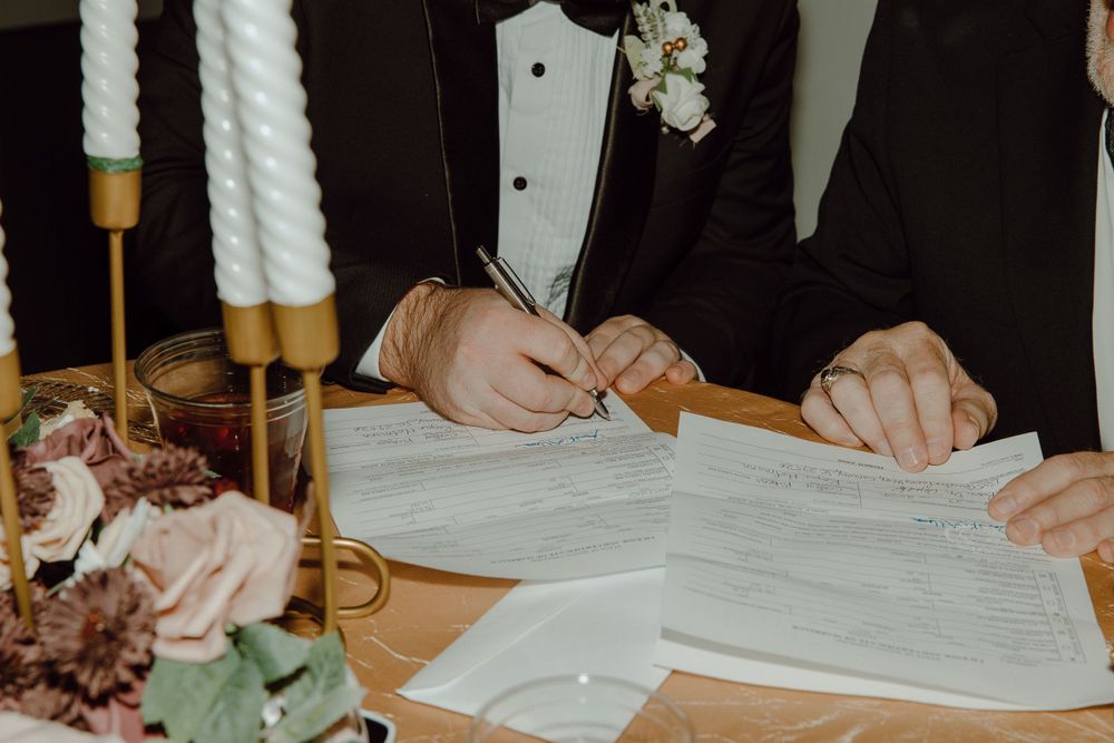 Wedding guests signing the marriage certificate at a table decorated with candles and flowers.