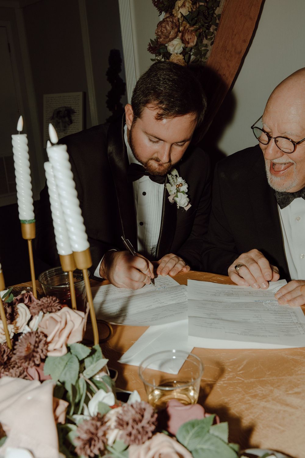 Guests signing documents at a wedding ceremony with floral decorations and candles.