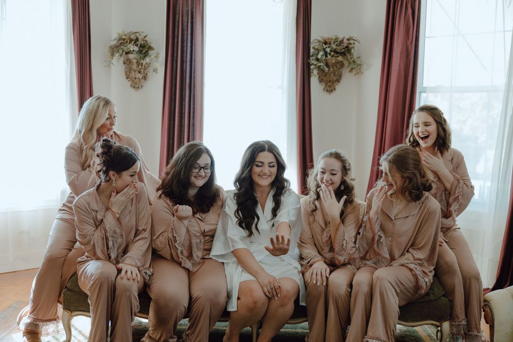 Wedding party in matching pink robes gathered together on a covered porch.