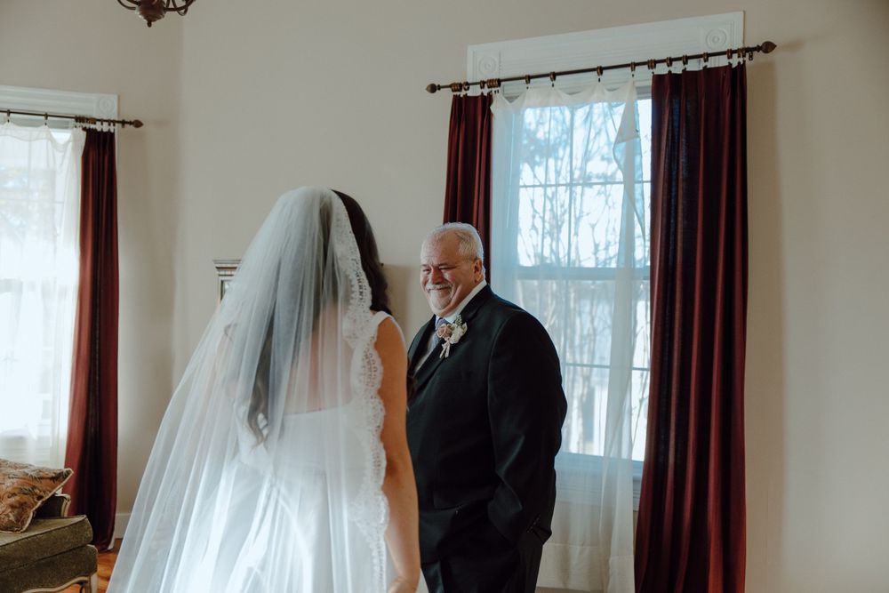 An intimate moment between bride and family member by a window with burgundy curtains.