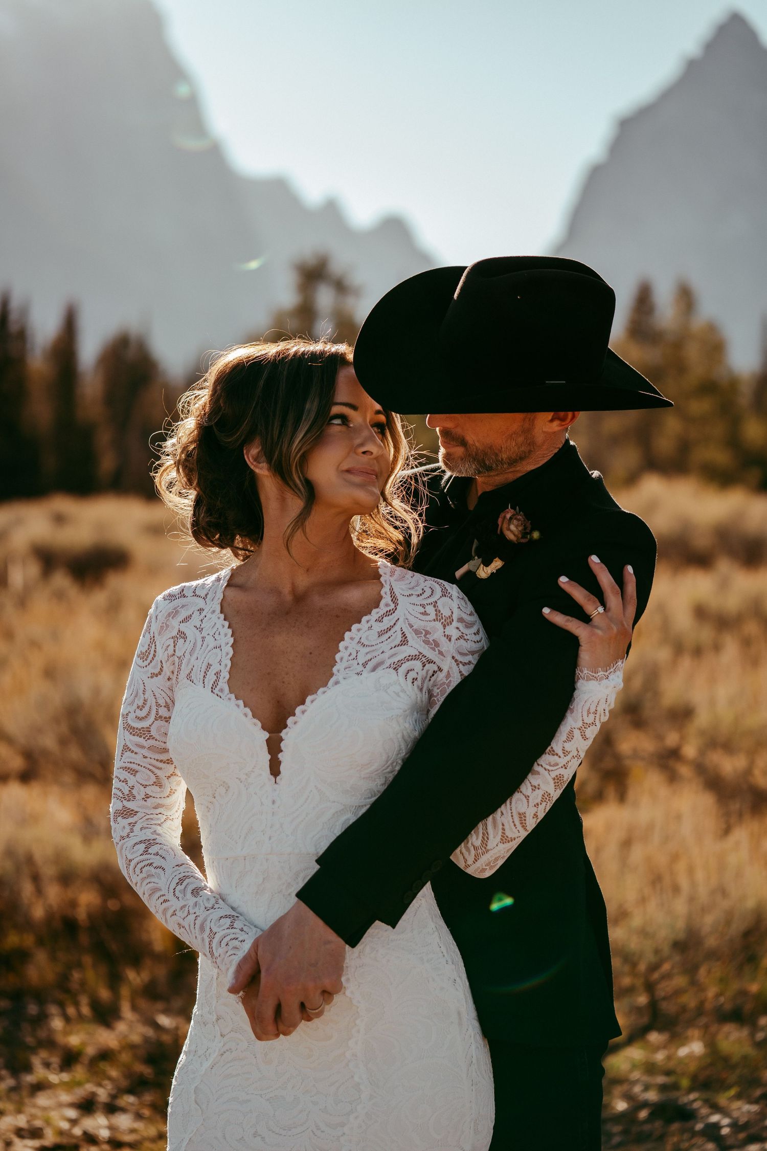 Romantic mountain wedding photo of a bride and groom sharing a kiss at sunset in a scenic meadow