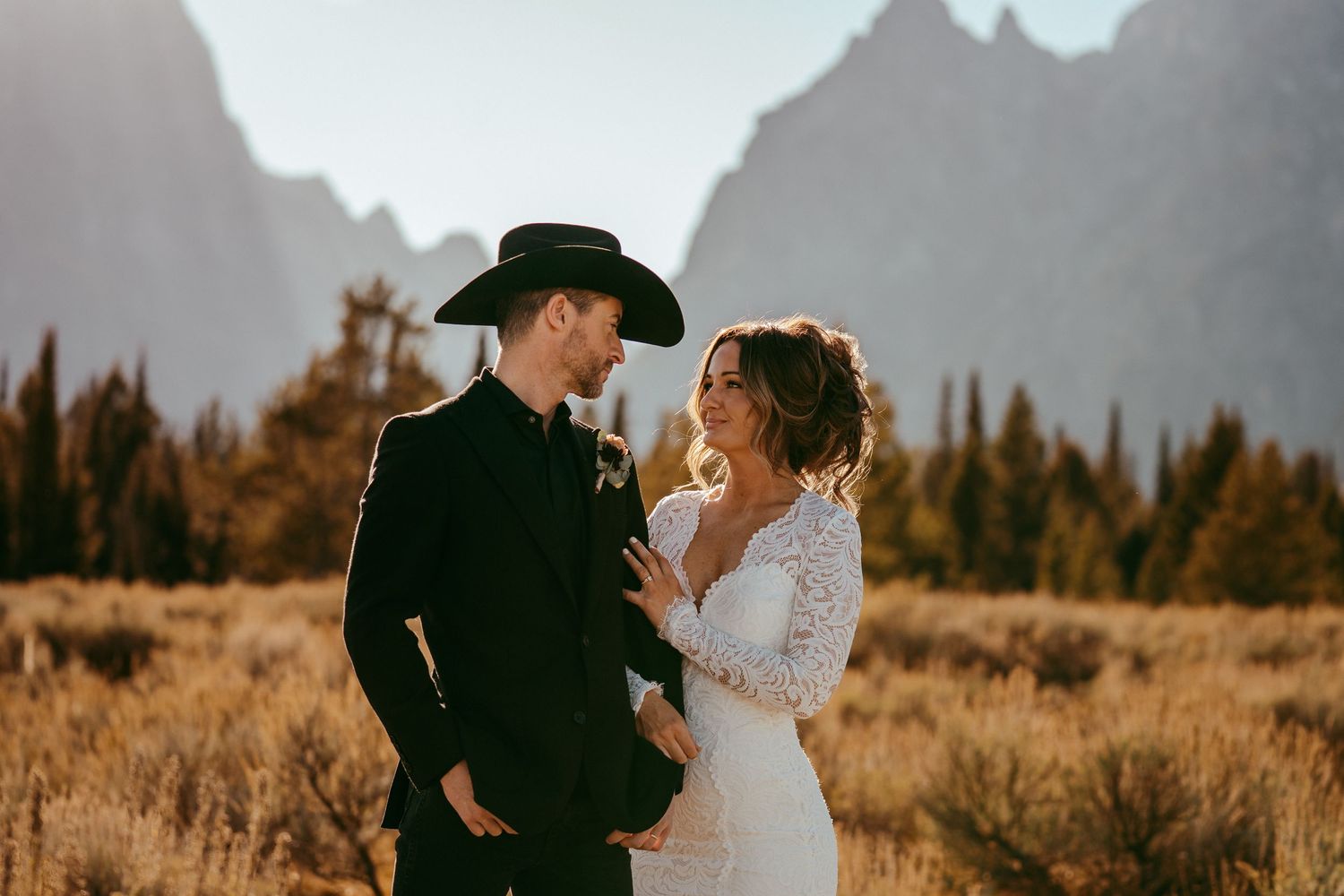 Romantic mountain wedding photo of a bride and groom sharing a kiss at sunset in a scenic meadow