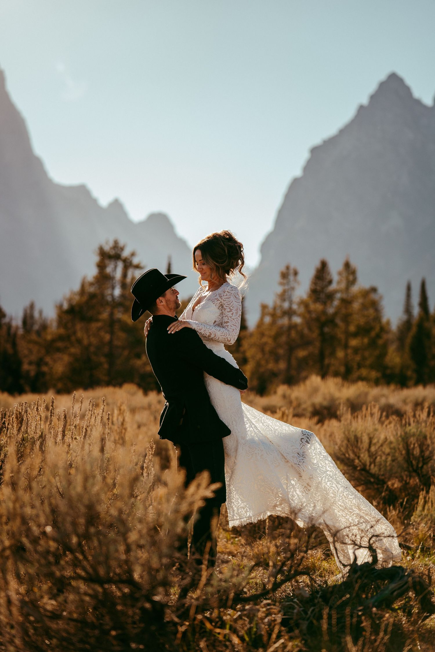 Romantic mountain wedding photo of a bride and groom sharing a kiss at sunset in a scenic meadow