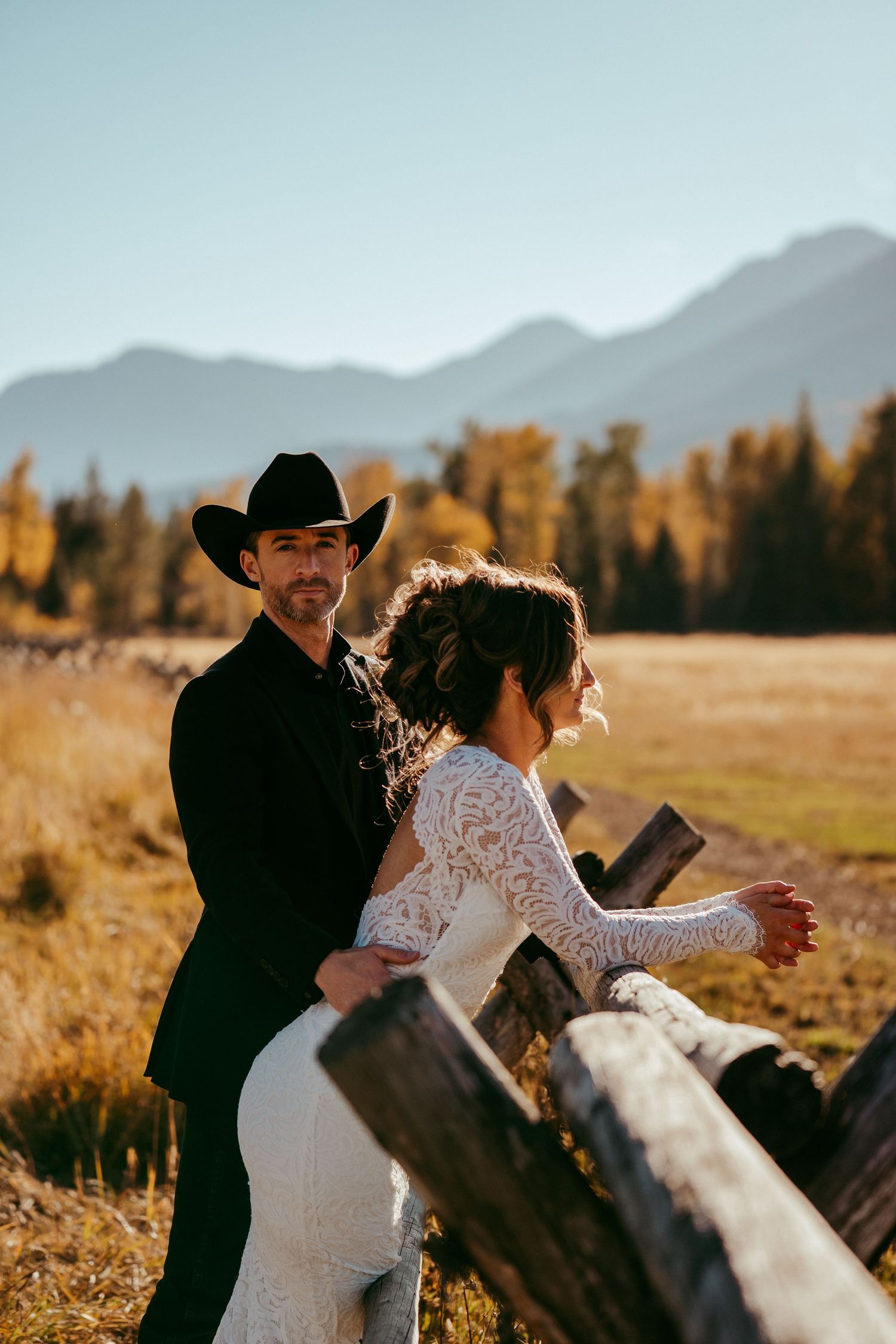 Romantic mountain wedding photo of a bride and groom sharing a kiss at sunset in a scenic meadow