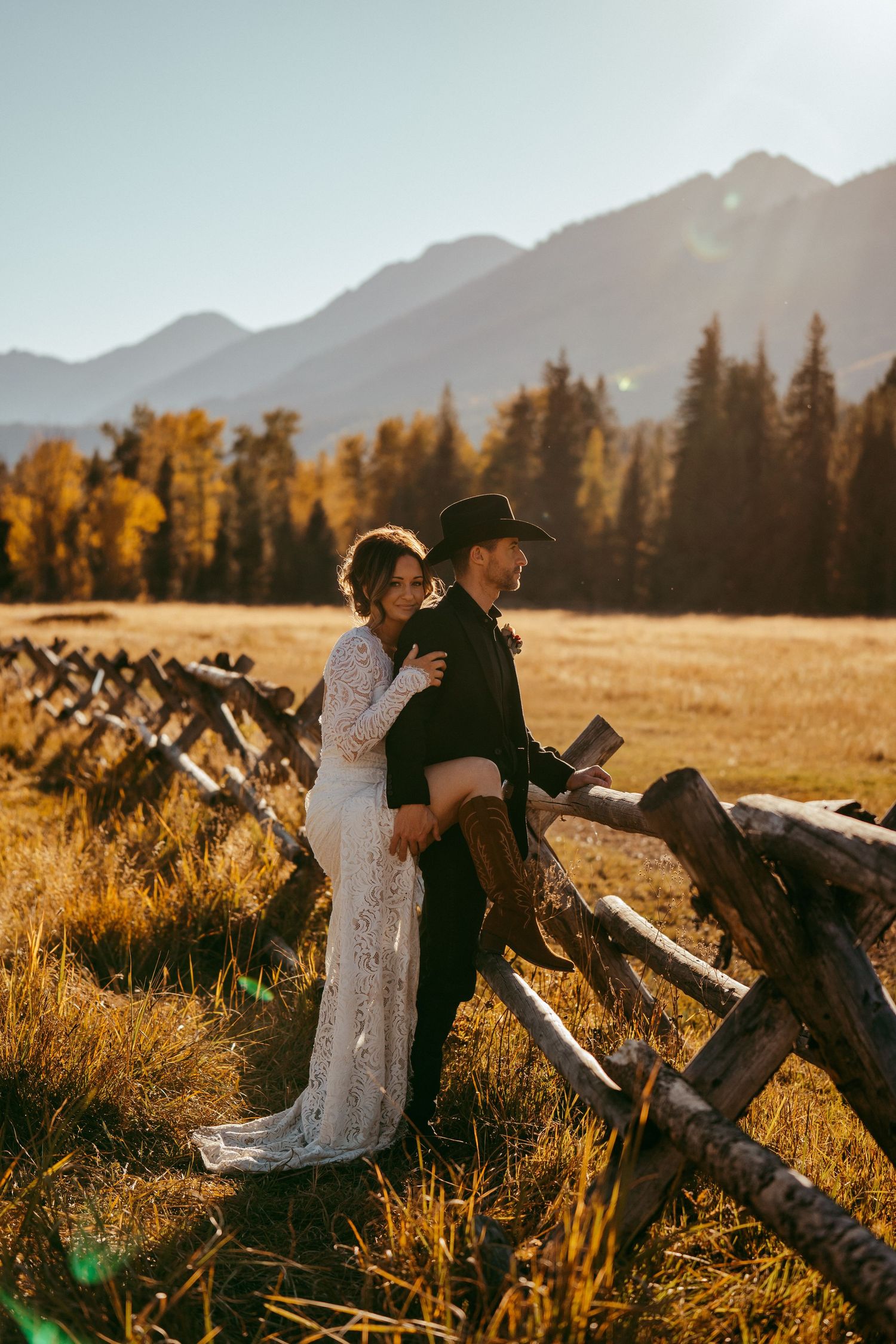 Romantic mountain wedding photo of a bride and groom sharing a kiss at sunset in a scenic meadow