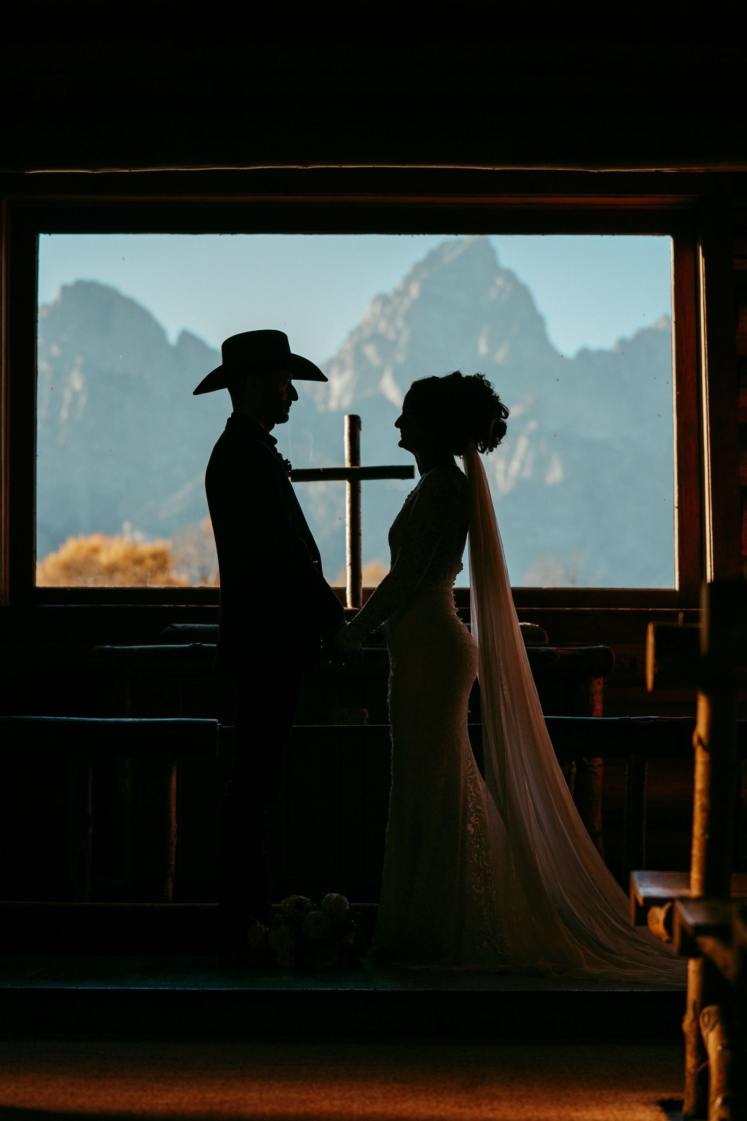Romantic mountain wedding photo of a bride and groom sharing a kiss at sunset in a scenic meadow