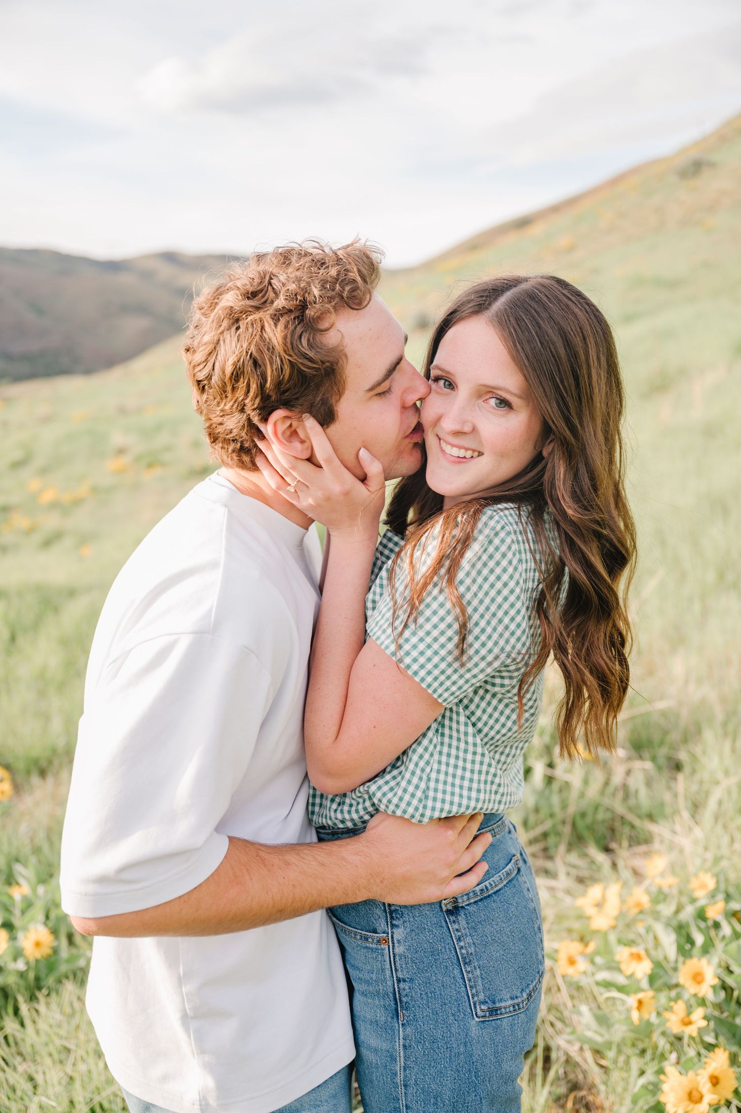 Couple embracing on large boulder in mountain forest setting at sunset.