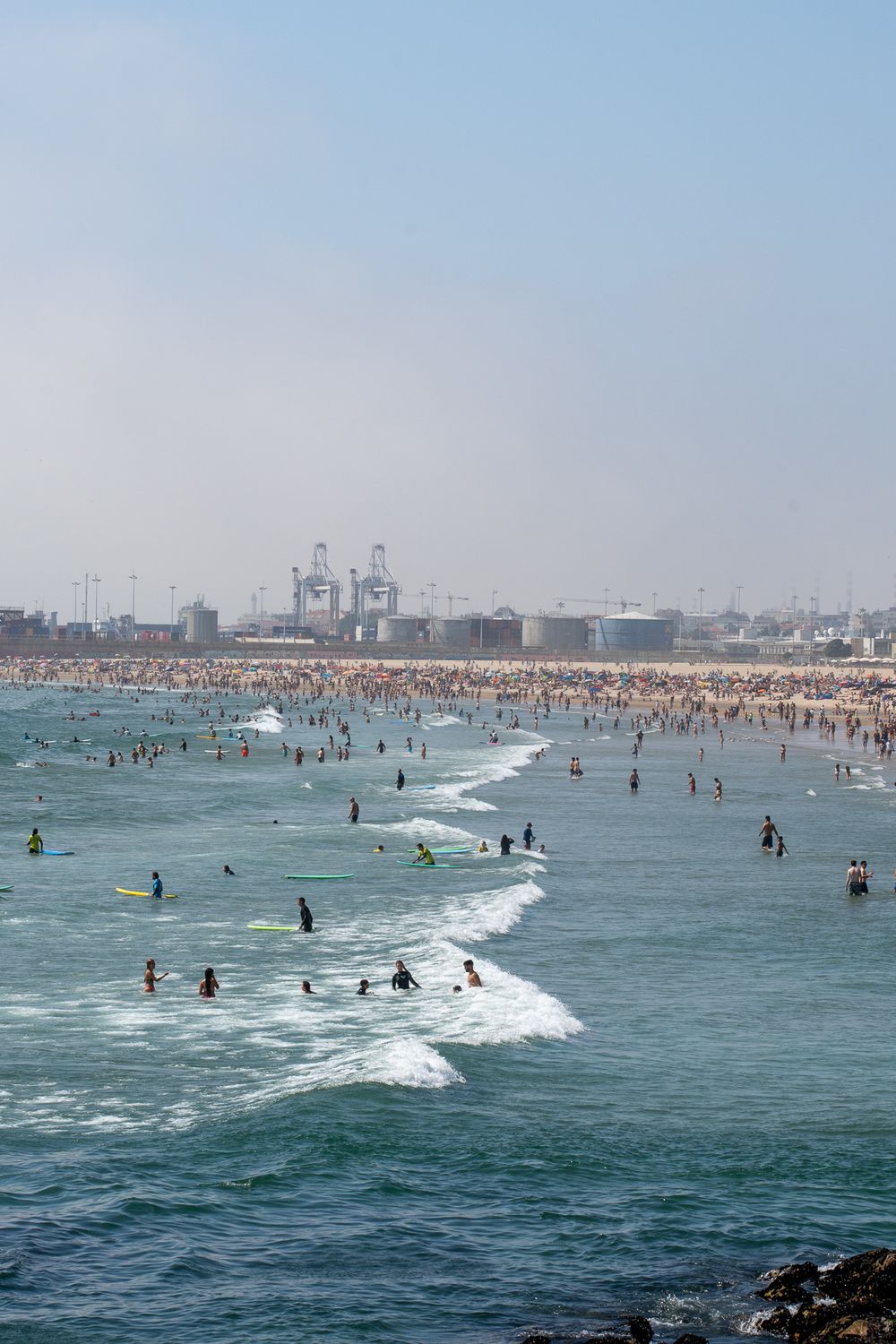 Crowded beach filled with swimmers enjoying the ocean waves on a sunny summer day.