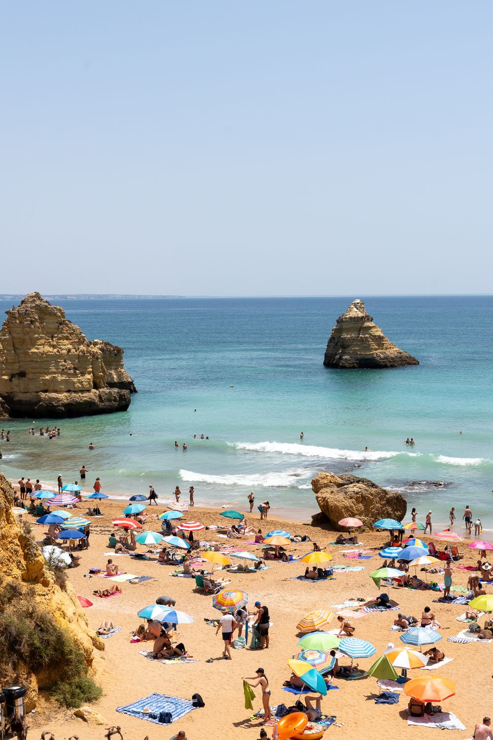 Scenic beach with limestone rock formations and colorful umbrellas dotting the sandy shoreline.