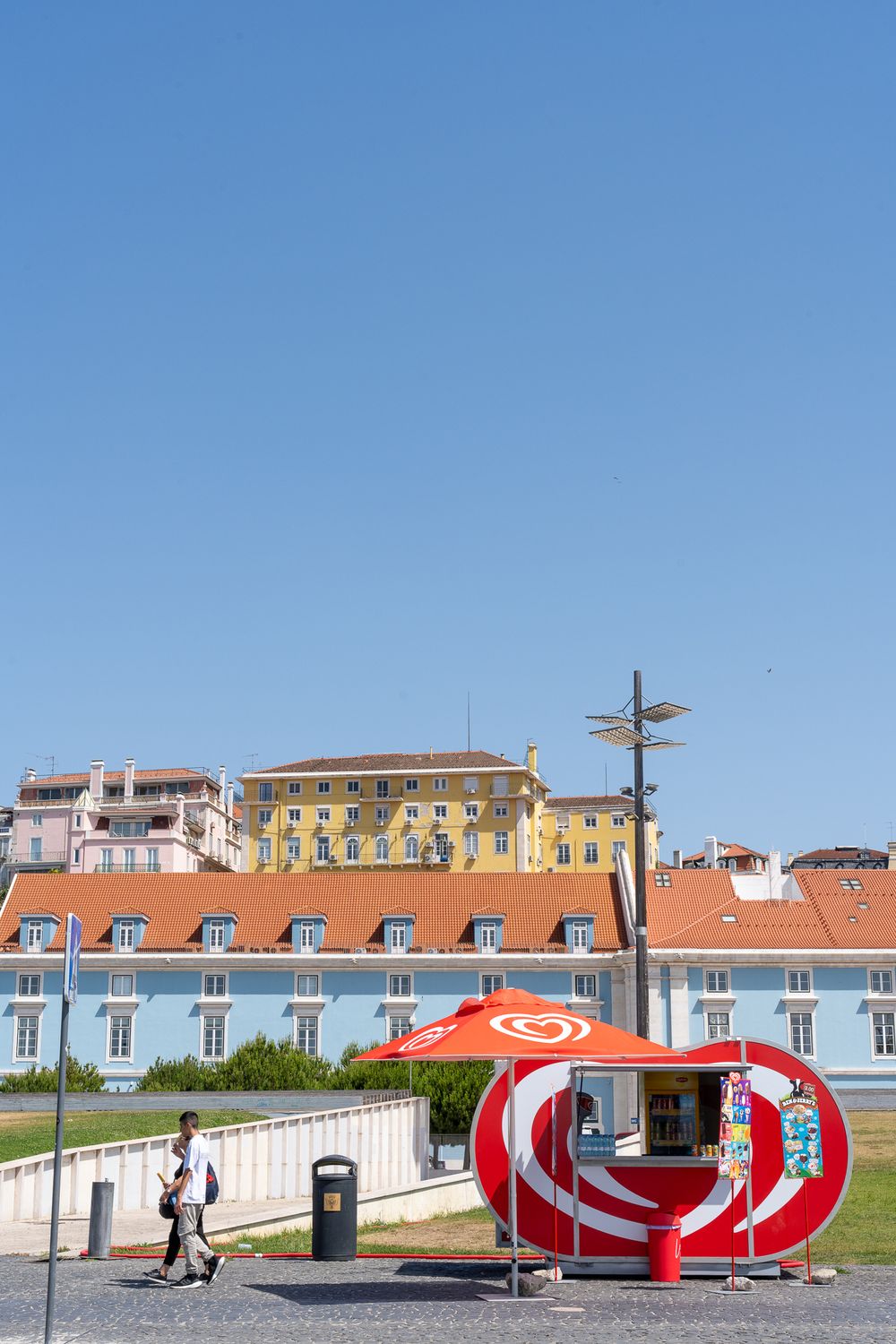 Colorful buildings on a hillside with a red modern bus shelter in the foreground.