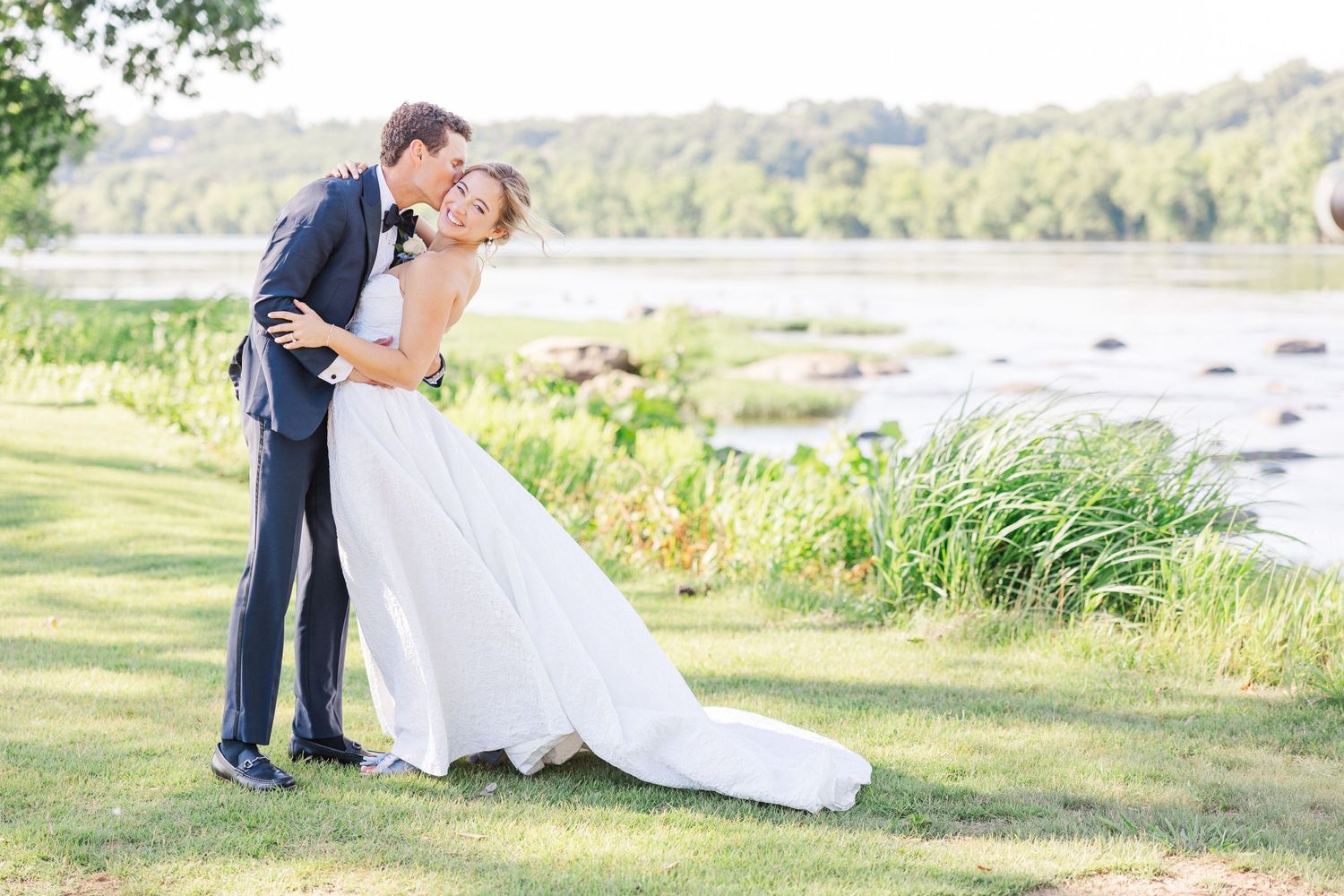 Wedding couple embracing by lakeside on sunny summer day.