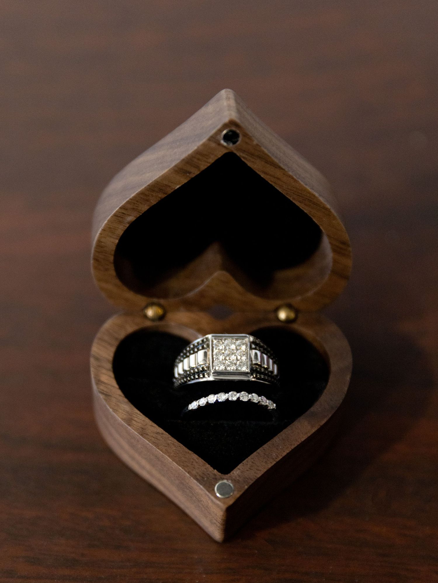 Diamond engagement ring nestled in heart-shaped wooden box with black velvet interior.