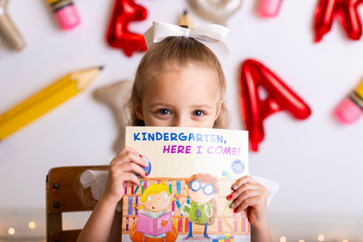 Student holding up kindergarten book against wall decorated with letters and pencils.