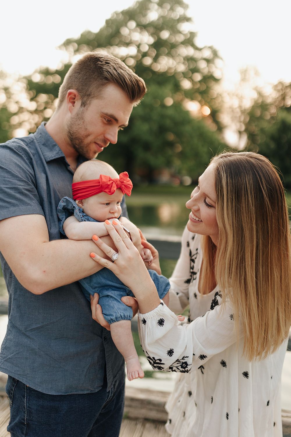 Young mom and dad smiling and interacting with their baby, with the dad holding their daughter and mom smiling happily.