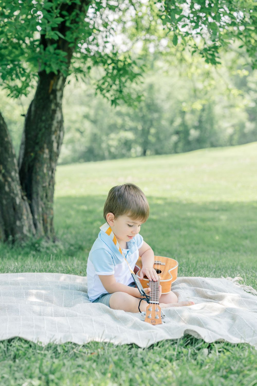 A young child sits on a blanket in the grass playing with toys on a sunny day.