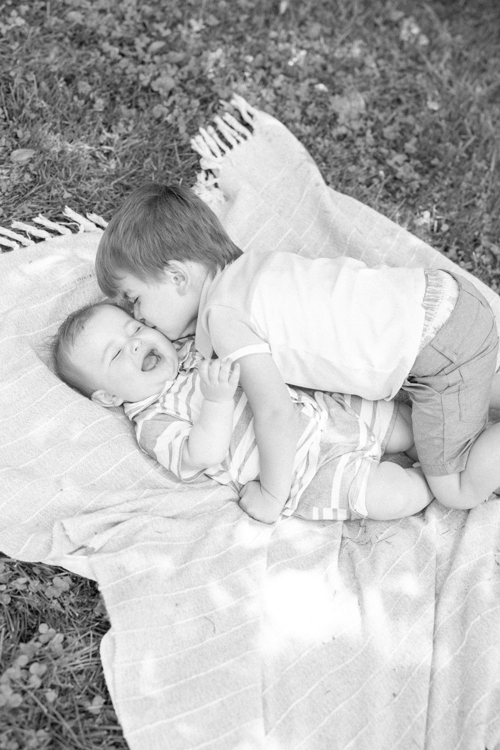 Two children share a sweet moment while resting on a blanket in black and white photography.