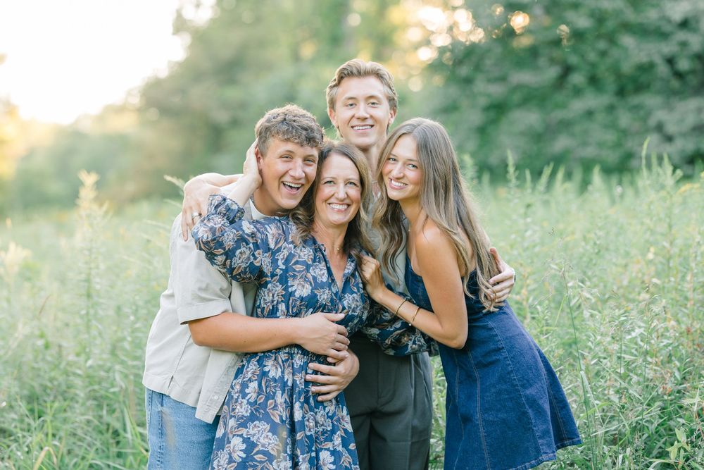 Family of four smiling and embracing in a sunlit green field during an outdoor portrait session.
