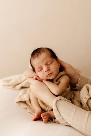 Sleeping newborn resting on gentle hands with cream blanket and neutral background.