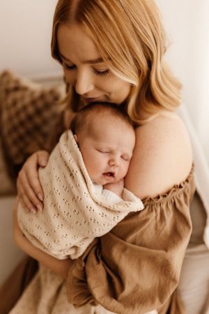 Intimate moment between caregiver and sleeping newborn in cream colored setting.