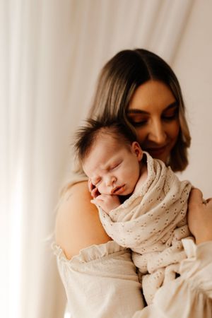 Intimate portrait of parent cradling sleeping newborn wrapped in cream colored swaddle.