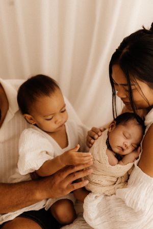 Family shares tender moment with newborn baby wrapped in cream blanket.